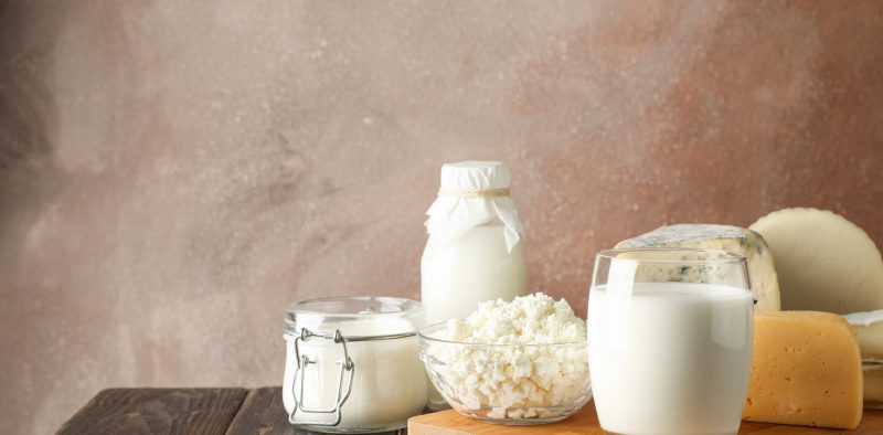 Fresh dairy products and cutting board on wooden background, copy space